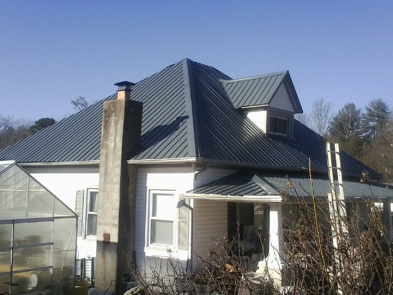 Dark blue standing seam metal roof on a white farmhouse with dormer — Slate & Tile Roof Repair by Roofing Brothers in New Canton