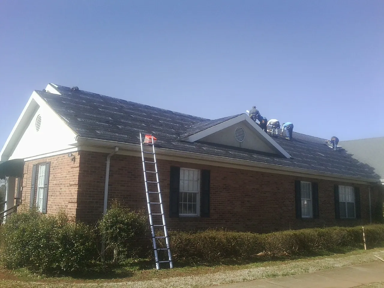 Crew tearing shingles off a brick ranch roof with a ladder set — Emergency Roof Repair work by our crew in New Canton