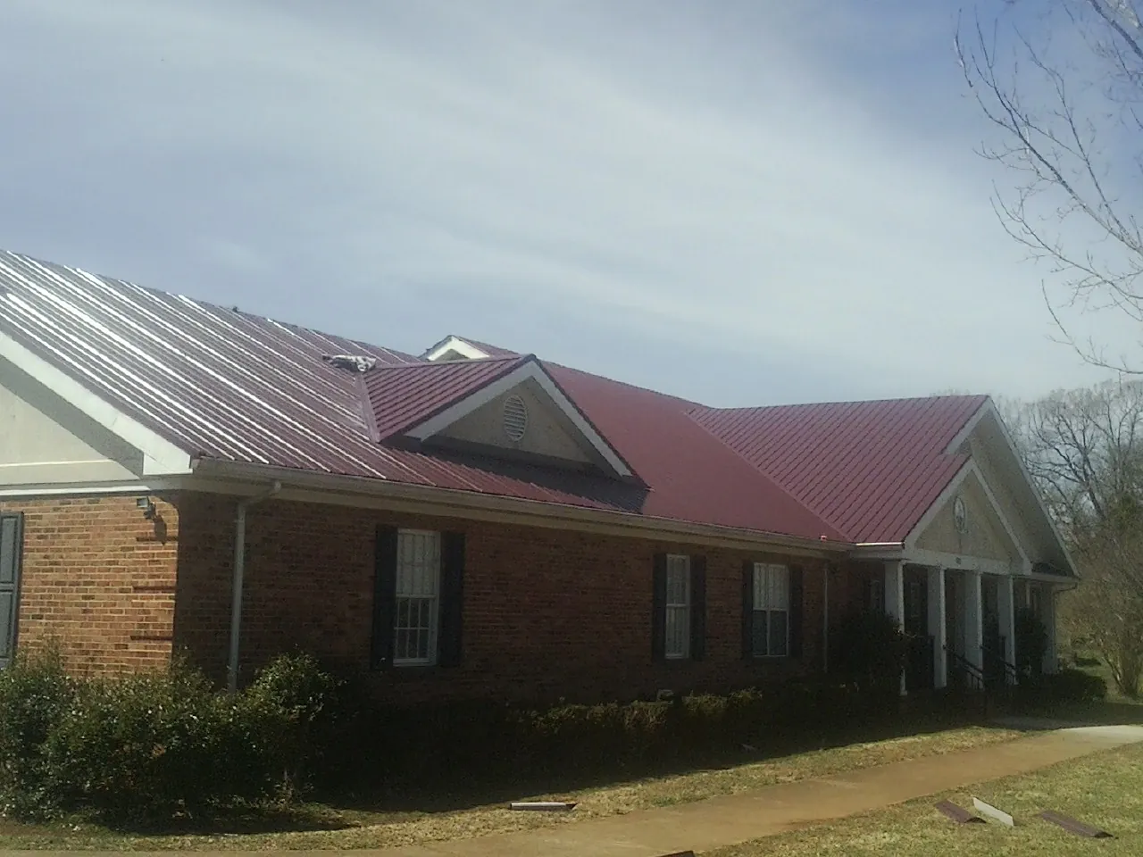 Red metal roof with gabled entries on a long brick building, from a Hail Damage Roof Repair job in New Canton