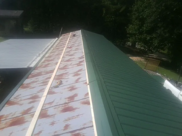 Old rusted panels beside newly installed green metal roofing — Wind Damage Roof Repair by Roofing Brothers in New Canton
