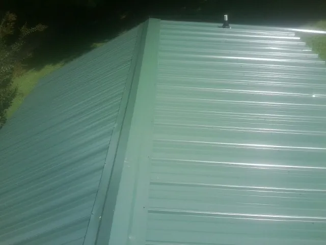 New green metal panels meeting at the ridge of a roof — Flat Roof Repair work by our crew in New Canton