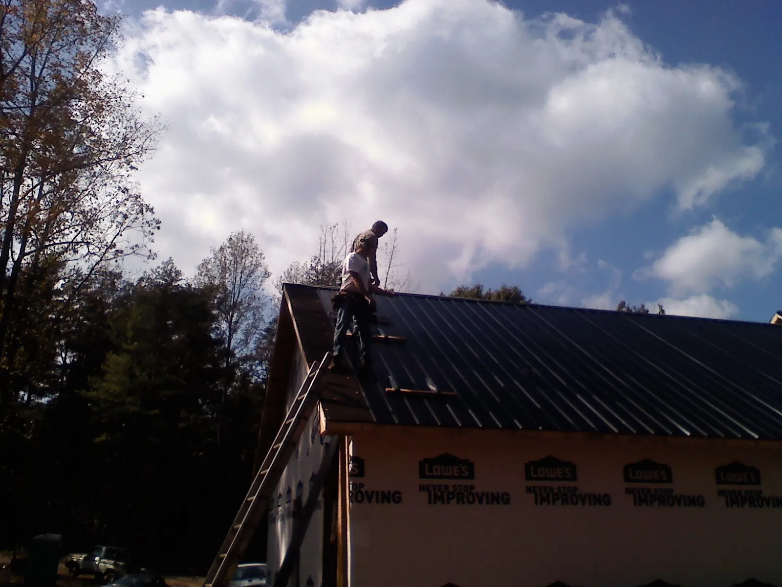 Roofer fastening dark metal panels high against a cloudy sky, from a Roof Inspection job in New Canton