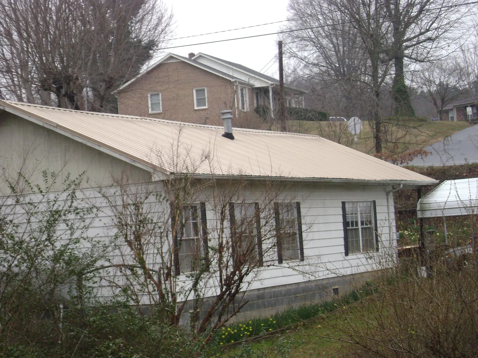 Tan metal roof on a white sided house set into a hillside — Commercial Roofing by Roofing Brothers in New Canton